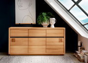 Houten dressoir met zes lades, versierd met een plant en een vaas, voor een donkere muur en een dakraam, gezien vanuit een vooraanzicht.