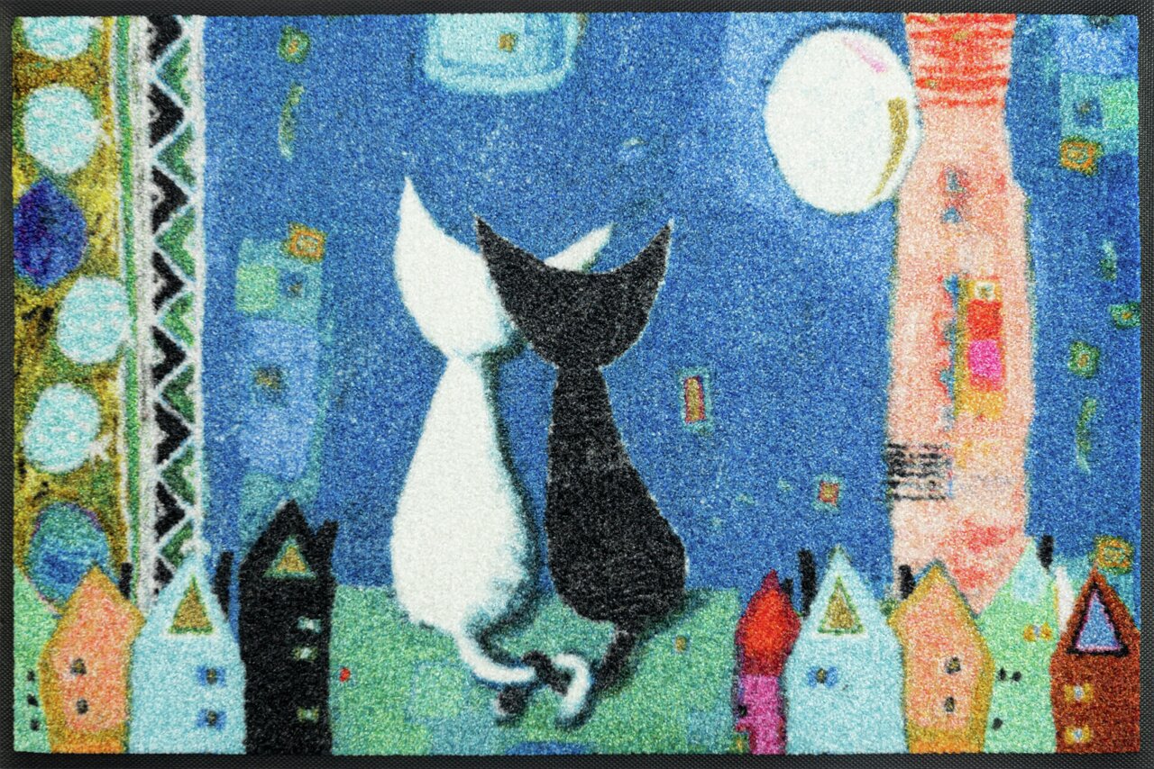 Teppich mit zwei Katzen, eine weiße und eine schwarze, die Rücken an Rücken unter einem Mond sitzen, umgeben von bunten Häusern und einem blauen Nachthimmel. Perspektive von oben.