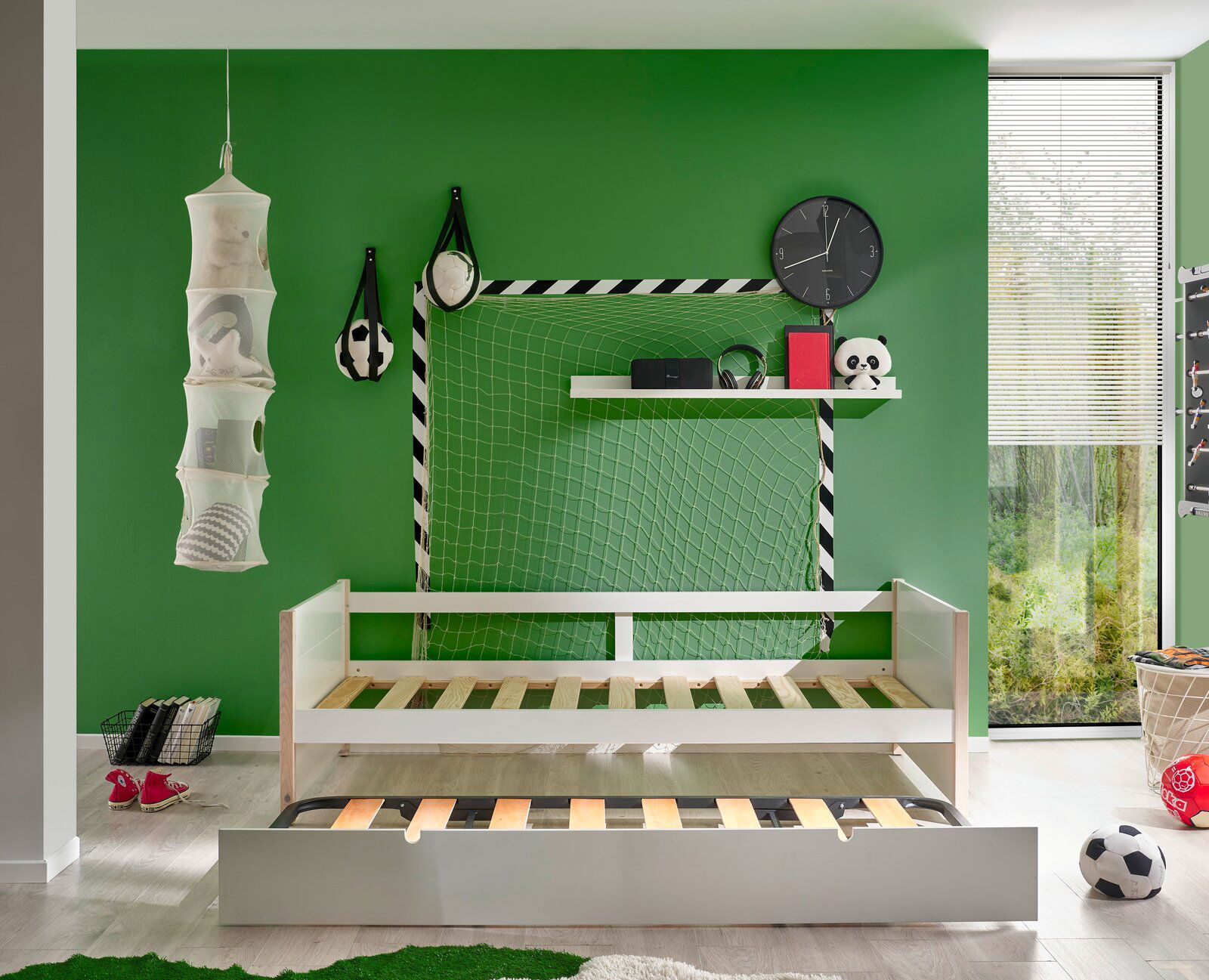 Jugendbett mit ausziehbarem Bettkasten, umgeben von sportlichen Dekorationen in einem grünen Zimmer, seitliche Perspektive