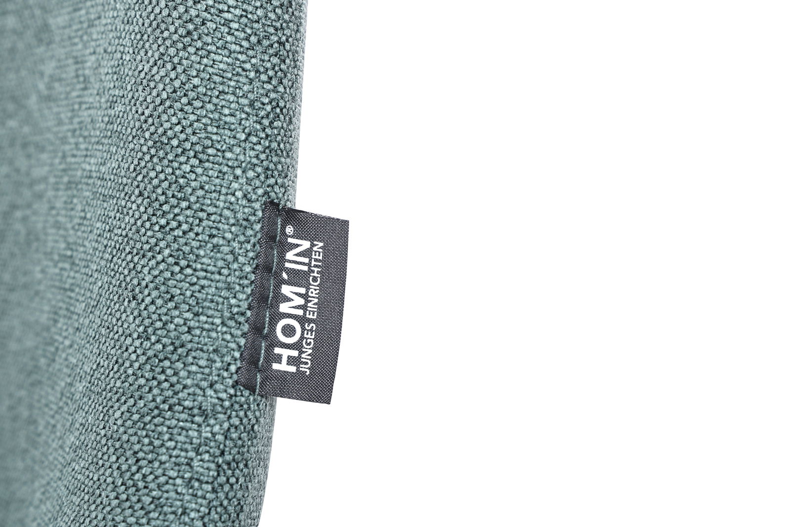 Nahaufnahme eines Stuhls mit grünem Stoffbezug und einem Etikett mit der Aufschrift 'HOM'IN Junges Einrichten'.