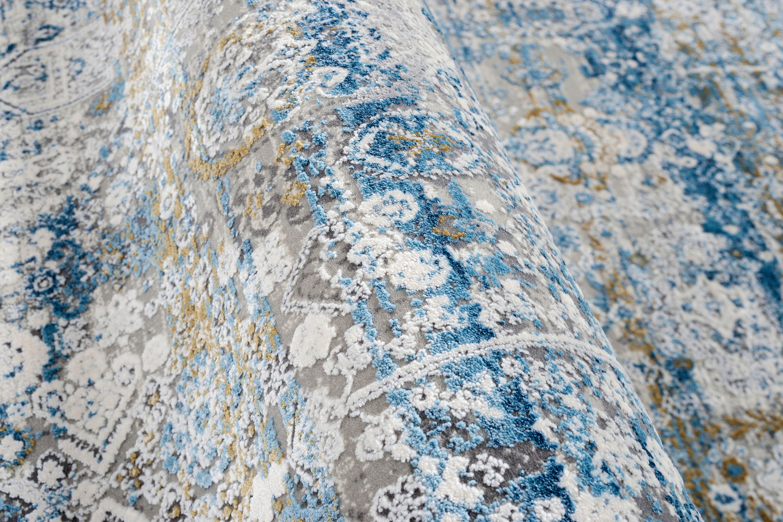 Nahaufnahme eines Designer-Teppichs mit blau-grauen und gelben Mustern, seitliche Perspektive