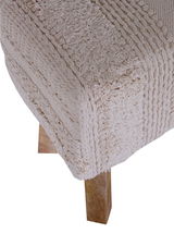 Nahaufnahme einer Hockerbank mit gestricktem, beigem Bezug und Holzbein, seitliche Perspektive