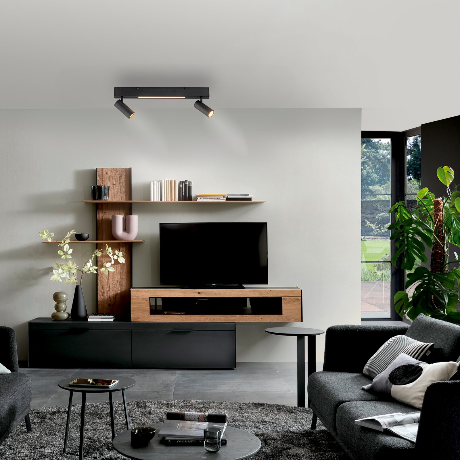 Schöner Wohnen LED-plafondlamp DANTE Modernes Wohnzimmer mit schwarzer Deckenleuchte mit zwei Spotstrahlern und Mittellicht über TV-Wandmöbel aus Holz und Schwarz; frontale Innenraumansicht auf die Szene.