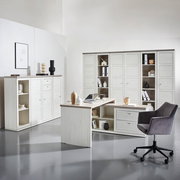 Moderner Eckschreibtisch in heller Holzoptik mit integriertem Stauraum, umgeben von passenden Schränken und einem grauen Bürostuhl, aus der Perspektive eines hellen, minimalistischen Büros.