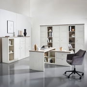 Moderner Eckschreibtisch in heller Holzoptik mit integriertem Stauraum, umgeben von passenden Schränken und einem grauen Bürostuhl, aus der Perspektive eines hellen, minimalistischen Büros.