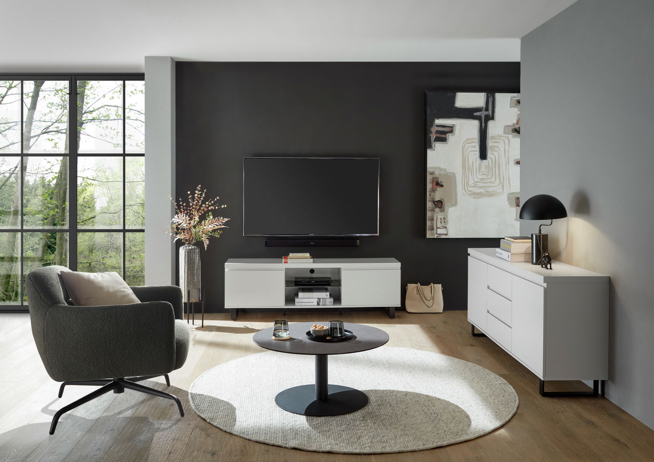 Modernes Wohnzimmer mit TV-Lowboard in Weiß, frontal betrachtet, neben einem Sideboard und einem gemütlichen Sessel.