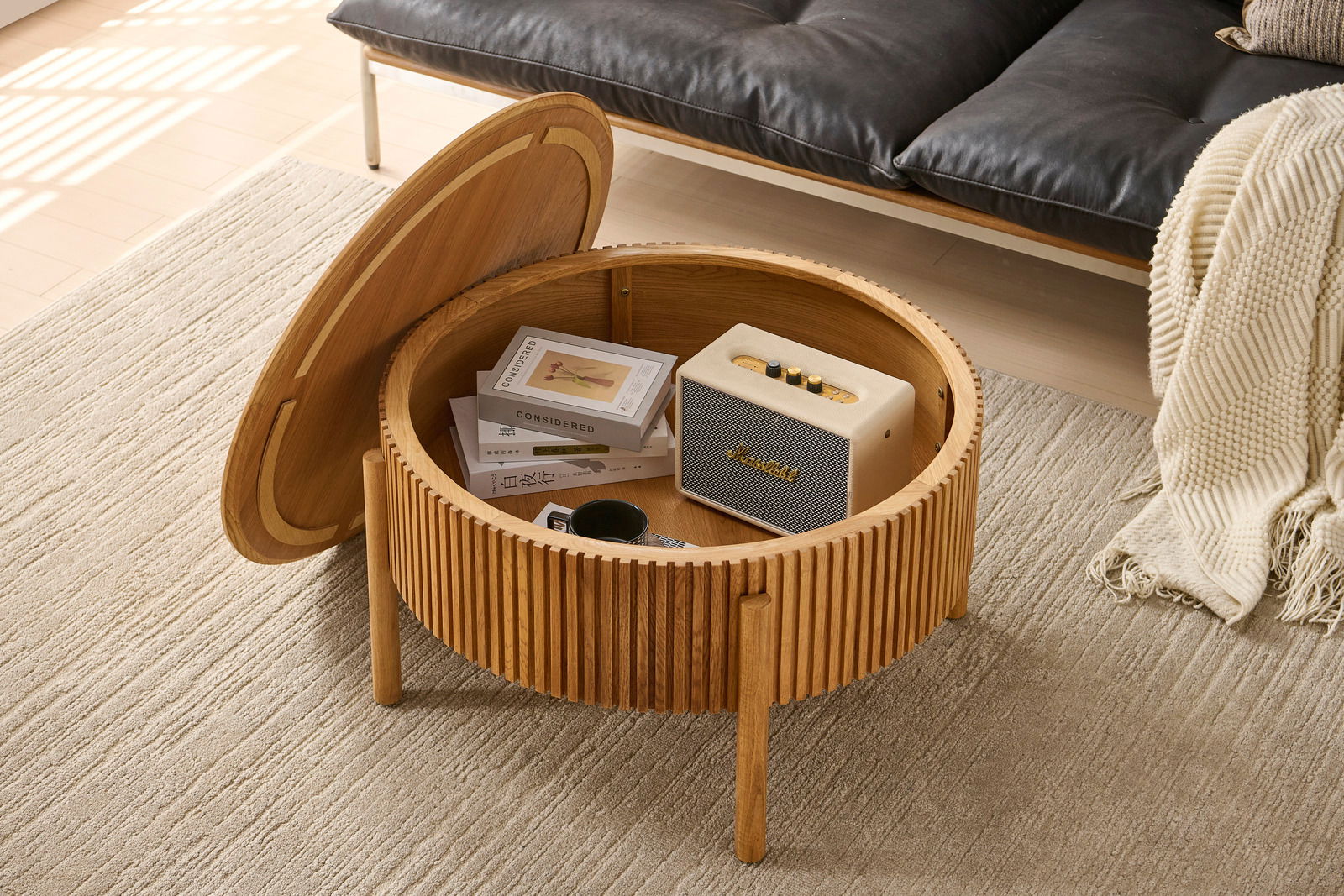 Runder Couchtisch aus Holz mit aufklappbarer Tischplatte, die Stauraum für Bücher und Lautsprecher bietet. Perspektive von oben.