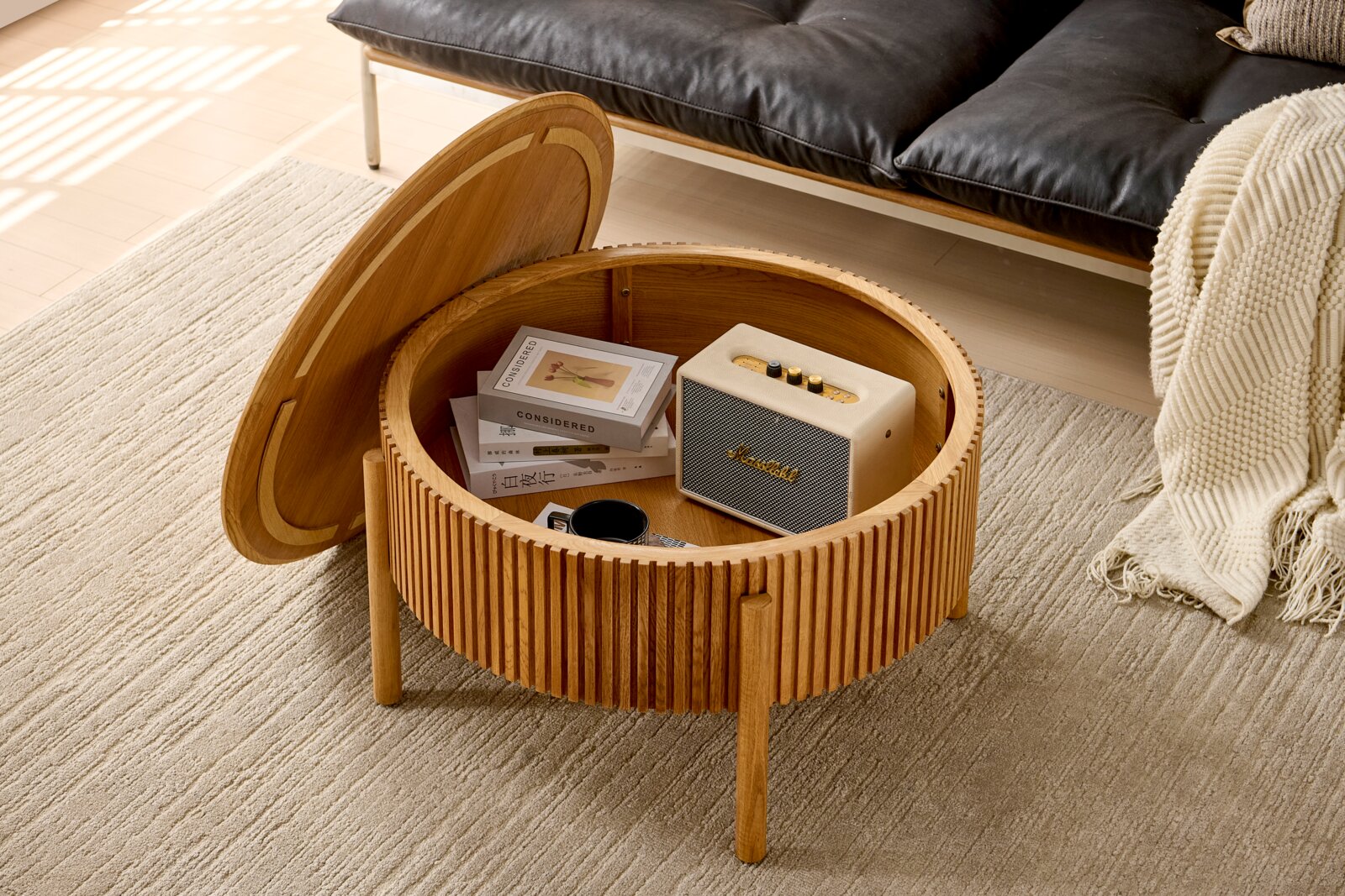 Runder Couchtisch aus Holz mit aufklappbarer Tischplatte, die Stauraum für Bücher und Lautsprecher bietet. Perspektive von oben.