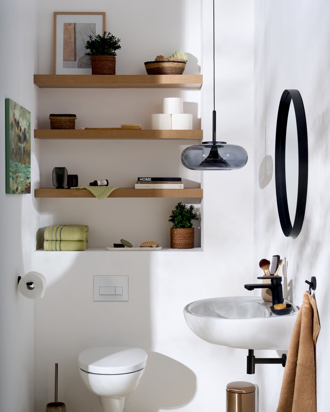 Frontale Raumansicht eines modernen, hellen Badezimmers mit weißem Wand-WC und Waschbecken, schwarzen Armaturen, ovalem Spiegel, Rauchglas-Pendelleuchte und dekorierten Holzregalen.