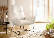 Moderner cremefarbener Sessel mit geripptem Stoffbezug und schwarzen Metallbeinen, seitliche Perspektive in einem hellen Raum mit großen Fenstern.