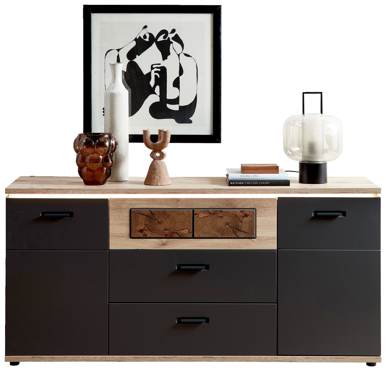 Moderne Kommode/Sideboard in Holzoptik mit mattschwarzen Fronten und Schubladen, dekoriert mit Vase, Glasobjekt, Skulptur, Büchern, Tischlampe und gerahmter Grafik; frontale Ansicht.