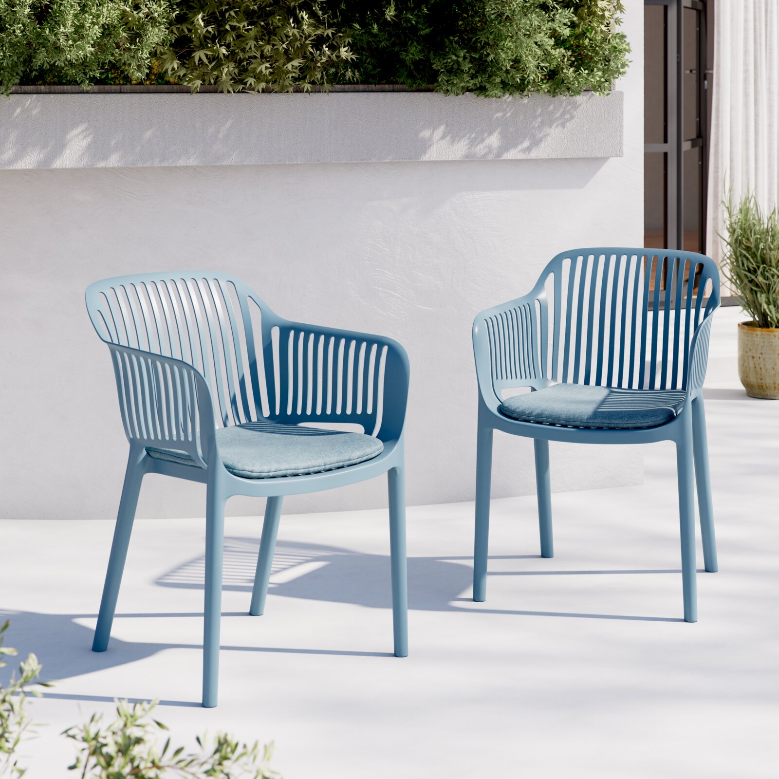 Zwei hellblaue Outdoor-Stühle aus Kunststoff mit geschlitzter Rückenlehne und passenden Sitzkissen auf einer sonnigen Terrasse vor weißer Wand und Pflanzkasten, Frontansicht in leichter Schrägperspektive.