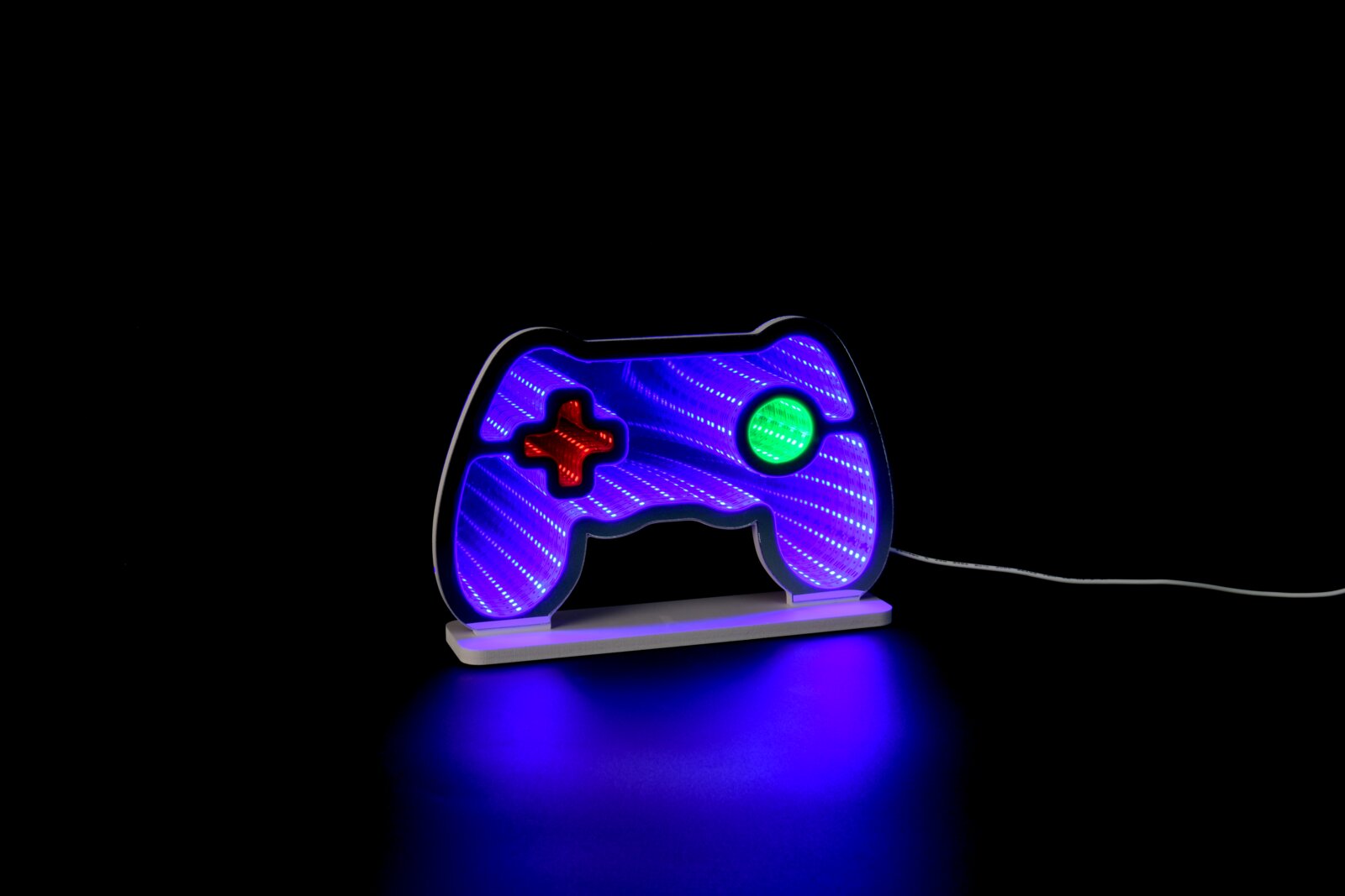 Novel LED-Dekoleuchte GAMER LED-Neonschild in Form eines Gamecontrollers mit blau-violetten Lichtstreifen, rotem Steuerkreuz und grünem Button auf weißem Sockel, mit Kabel nach rechts; frontal in leichter Seitenperspektive vor schwarzem Hintergrund