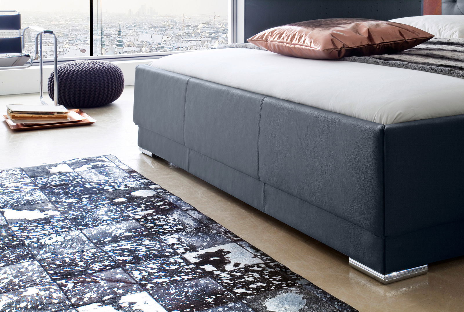 Seitliche Perspektive auf ein modernes Polsterbett in einem stilvollen Raum mit Stadtblick.