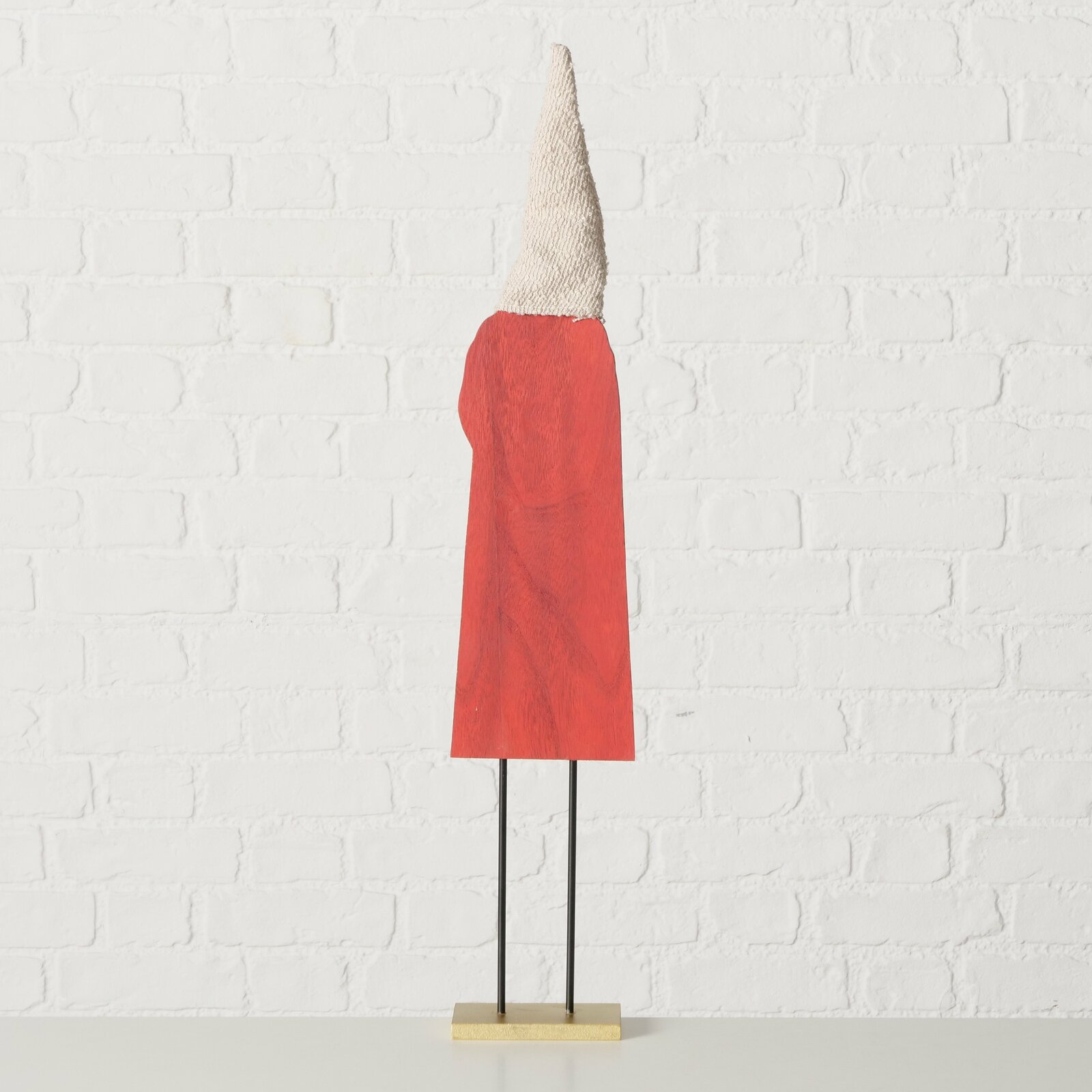 Figur mit rotem Umhang und spitzem, strukturiertem Hut, von hinten betrachtet, auf einem Sockel stehend.