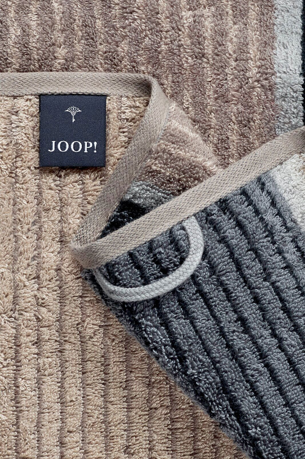 Nahaufnahme eines JOOP! Handtuchs aus der SIGNATURE Kollektion in verschiedenen Brauntönen mit sichtbarem Etikett. Perspektive von oben.