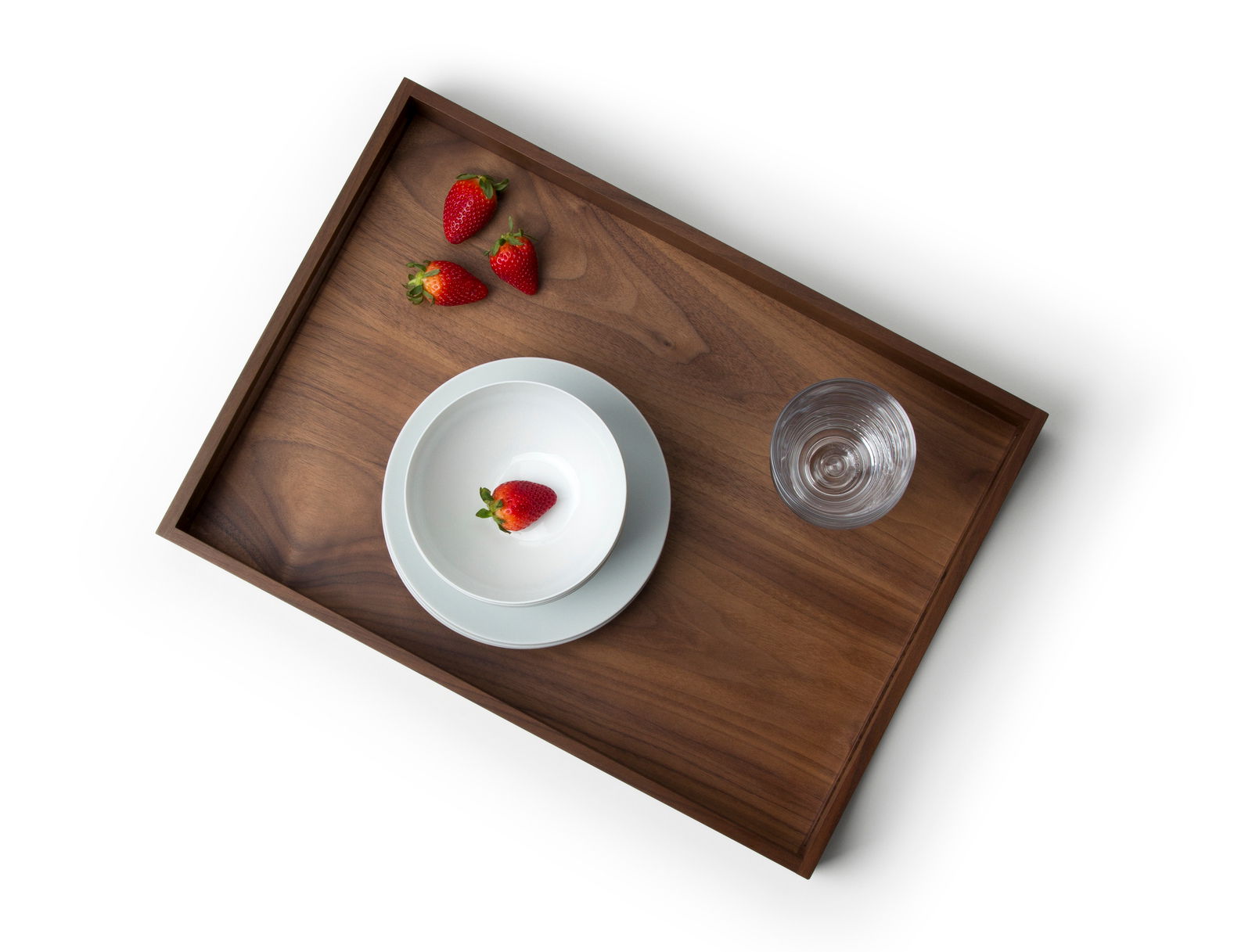 Vogelperspektive auf ein Tablett aus Walnussholz mit einer Schale, einem Glas und Erdbeeren.