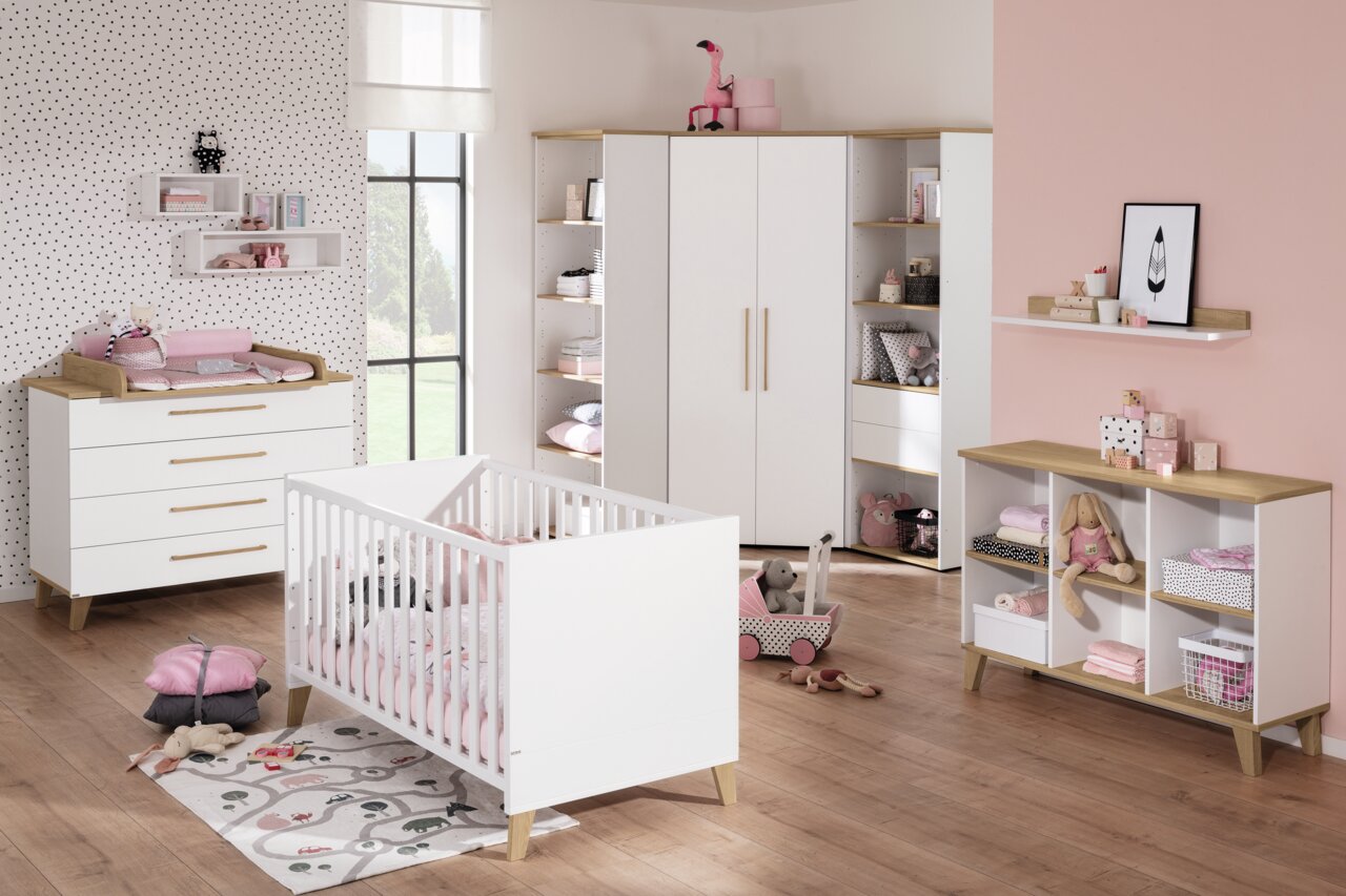 Modernes Kinderzimmer mit weißem Kinderbett aus Holz, umgeben von stilvollen Möbeln in einem hellen Raum mit rosa Akzenten, aus der Perspektive von vorne.