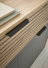 Nahaufnahme einer modernen Kommode mit Holzlamellen und schwarzen Griffen, von oben betrachtet.