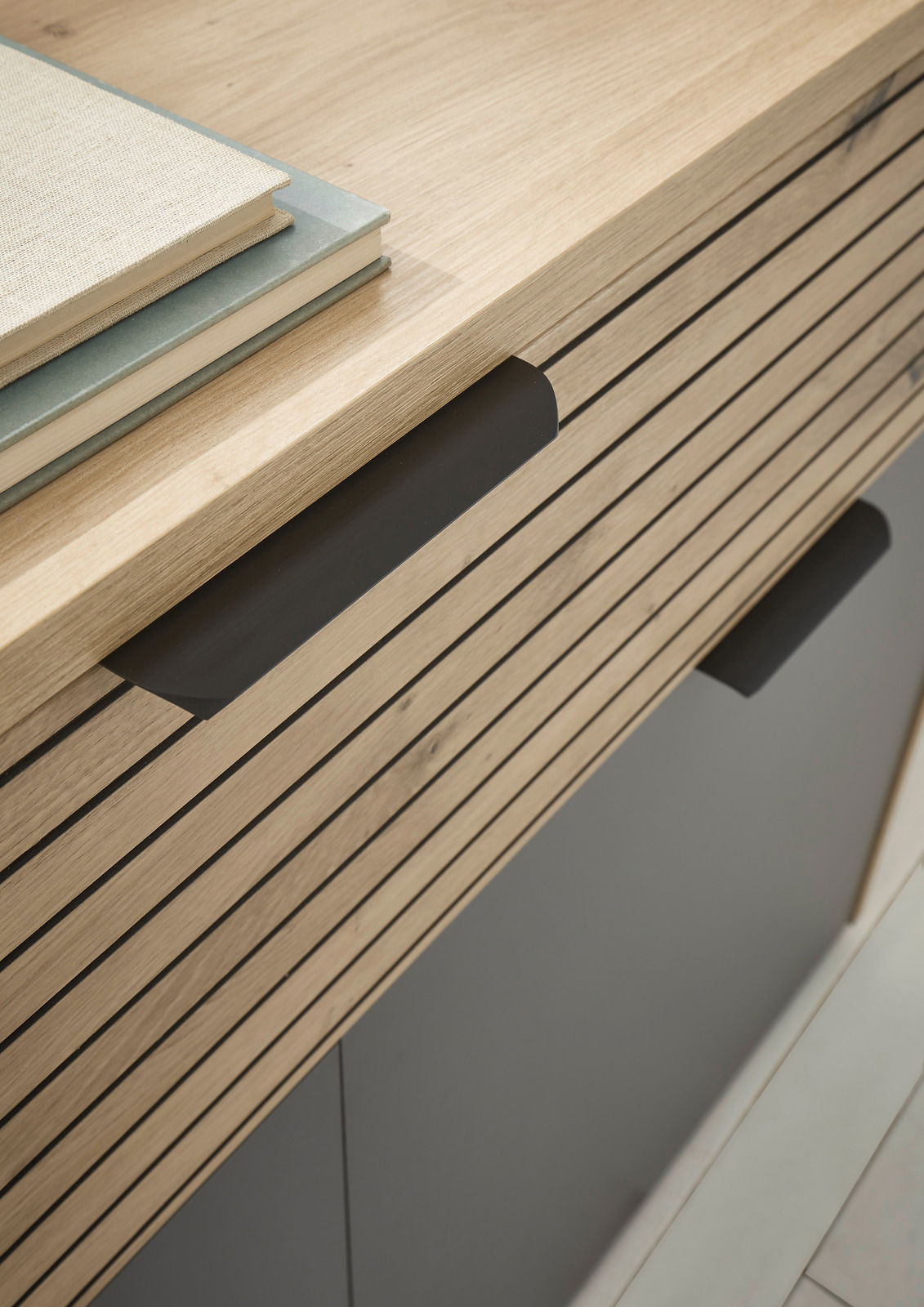 Nahaufnahme einer modernen Kommode mit Holzlamellen und schwarzen Griffen, von oben betrachtet.
