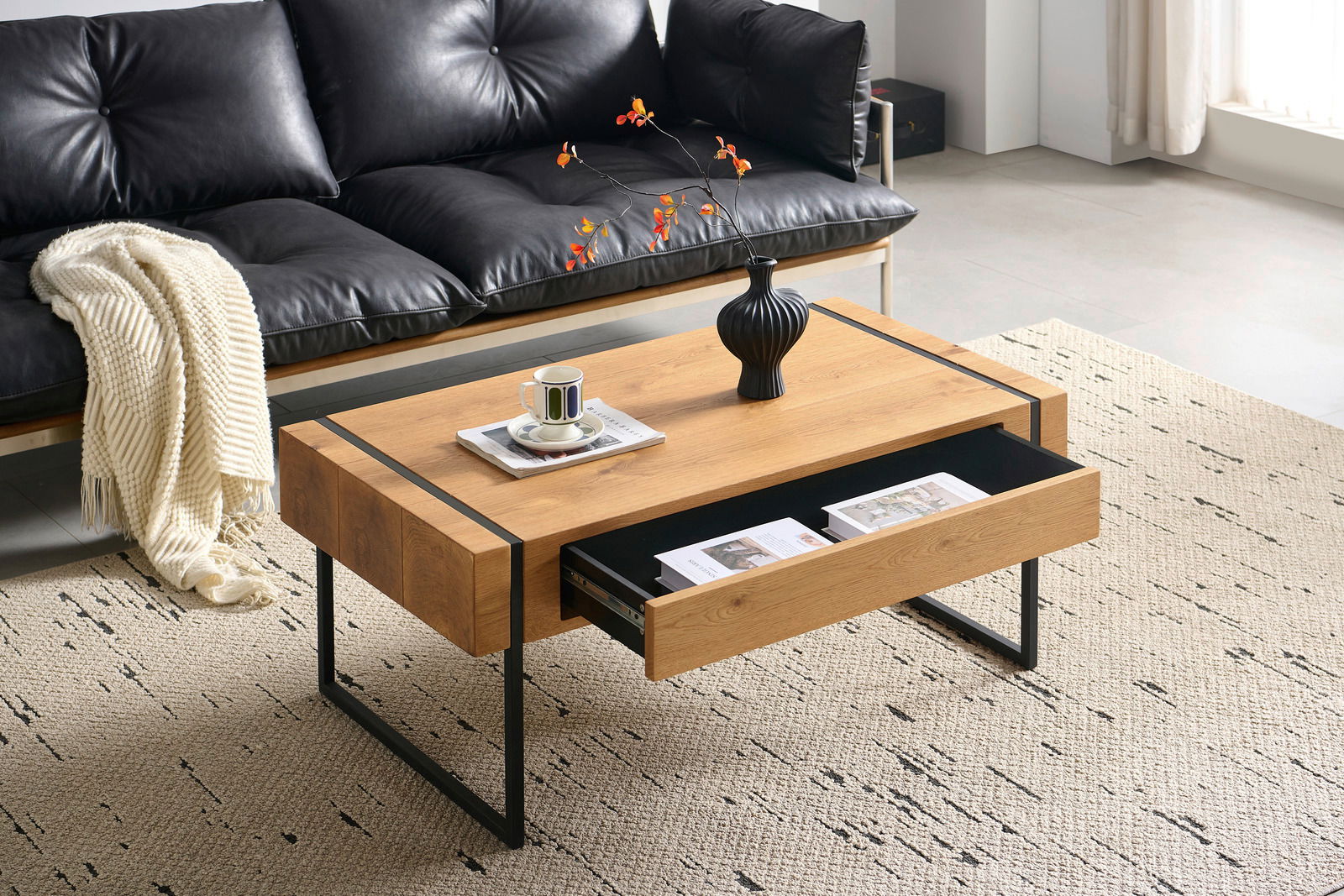 Moderner Couchtisch aus Holz mit schwarzem Metallgestell, Schublade geöffnet, von schräg oben fotografiert, dekoriert mit Vase und Tasse.