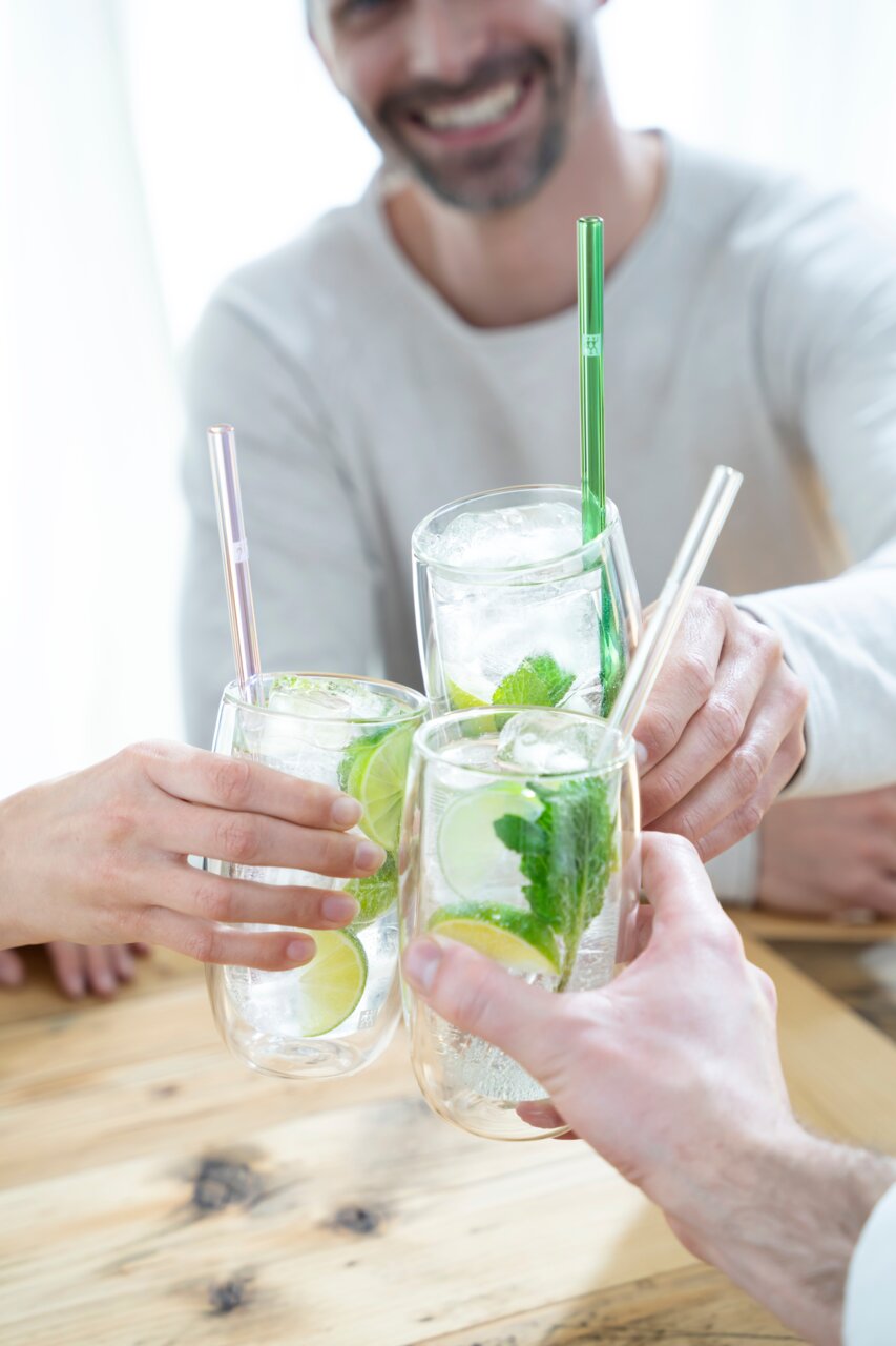 Vier personen proosten met glazen latte macchiato, gevuld met drank, schijfjes limoen en muntblaadjes, gezien vanuit vogelperspectief.