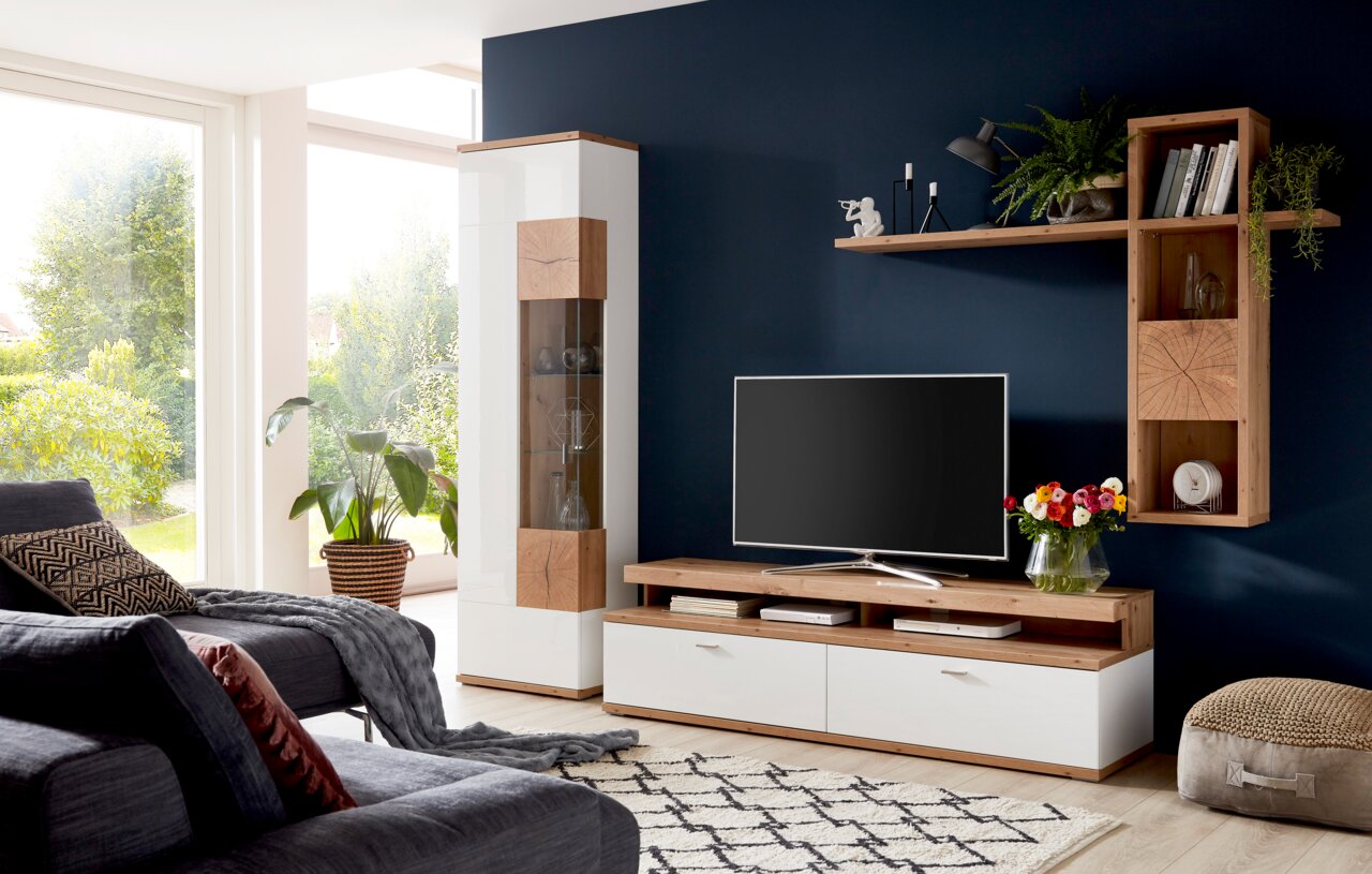 Moderne Wandkombination in einem Wohnzimmer mit weißem und holzfarbenem Design, bestehend aus einem TV-Schrank, einem hohen Schrank und einem Wandregal. Perspektive von vorne.