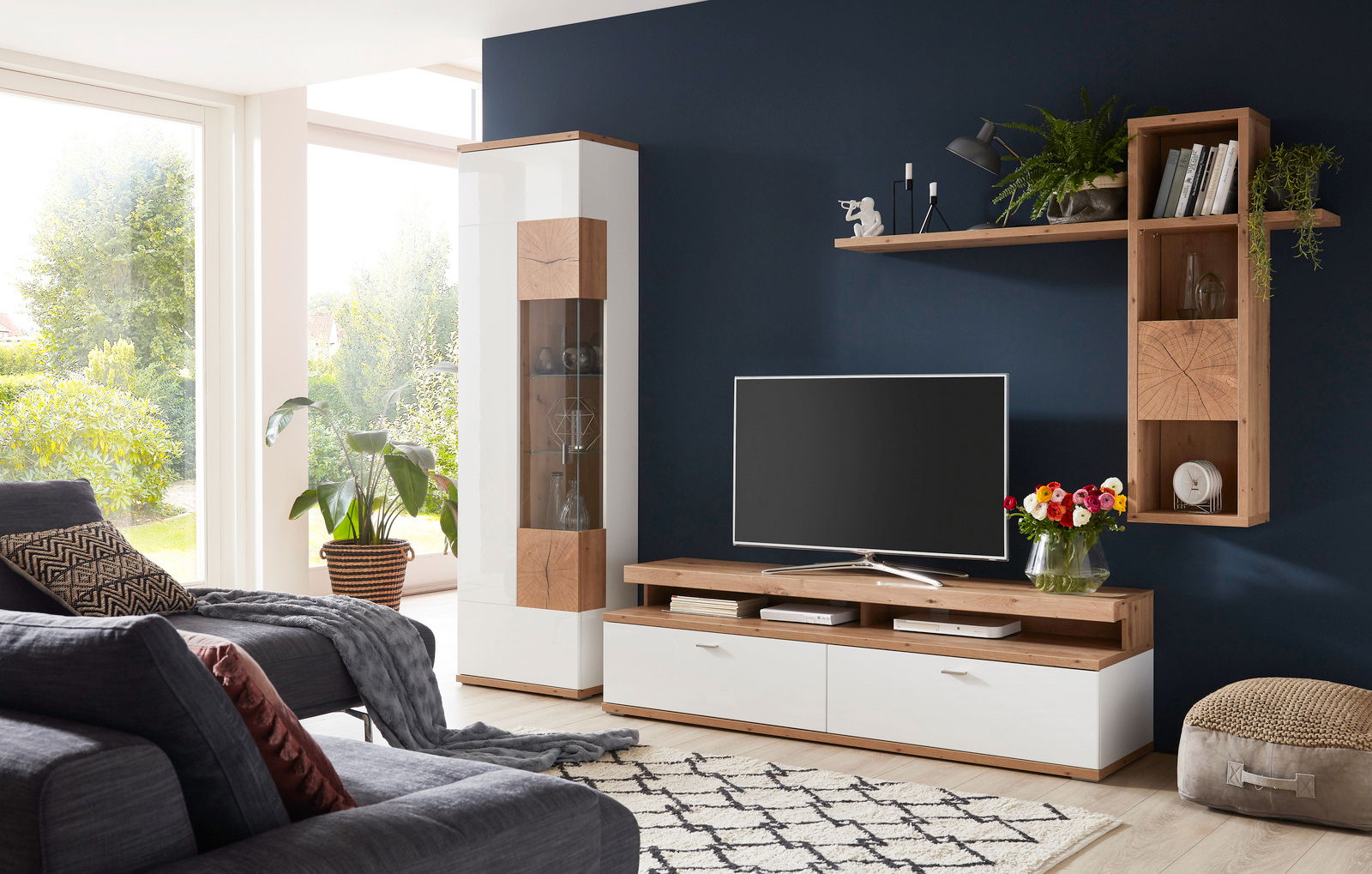 Moderne Wandkombination in einem Wohnzimmer mit weißem und holzfarbenem Design, bestehend aus einem TV-Schrank, einem hohen Schrank und einem Wandregal. Perspektive von vorne.