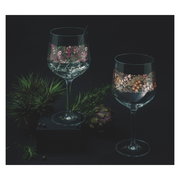 Zwei elegante Weingläser mit floralen Mustern, umgeben von Pflanzen, aus der Perspektive leicht von oben betrachtet.
