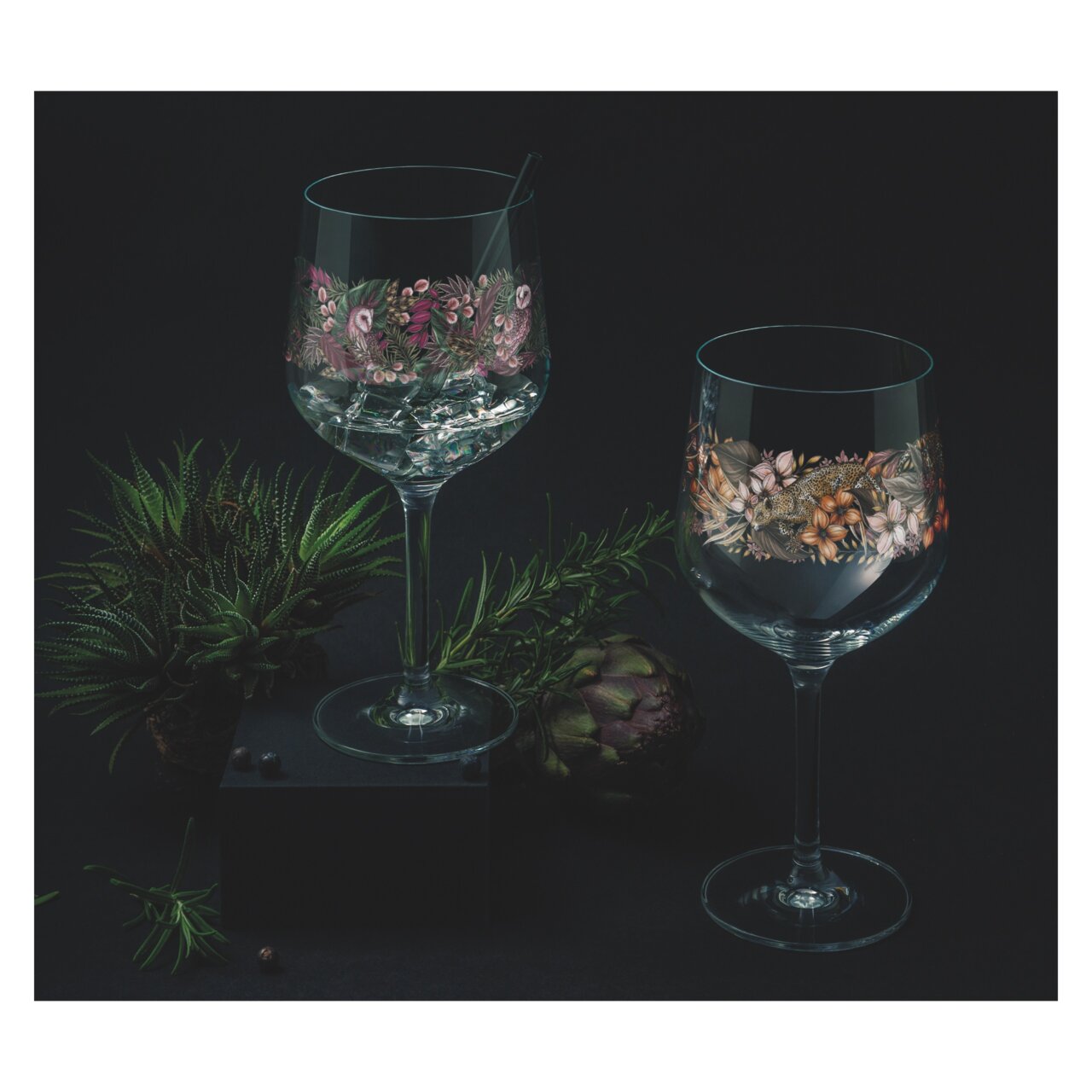 Zwei elegante Weingläser mit floralen Mustern, umgeben von Pflanzen, aus der Perspektive leicht von oben betrachtet.