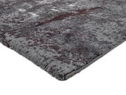 Nahaufnahme eines grauen Teppichs mit abstraktem Muster in verschiedenen Grautönen und einem Hauch von Rot, perspektivisch von der Seite aufgenommen.