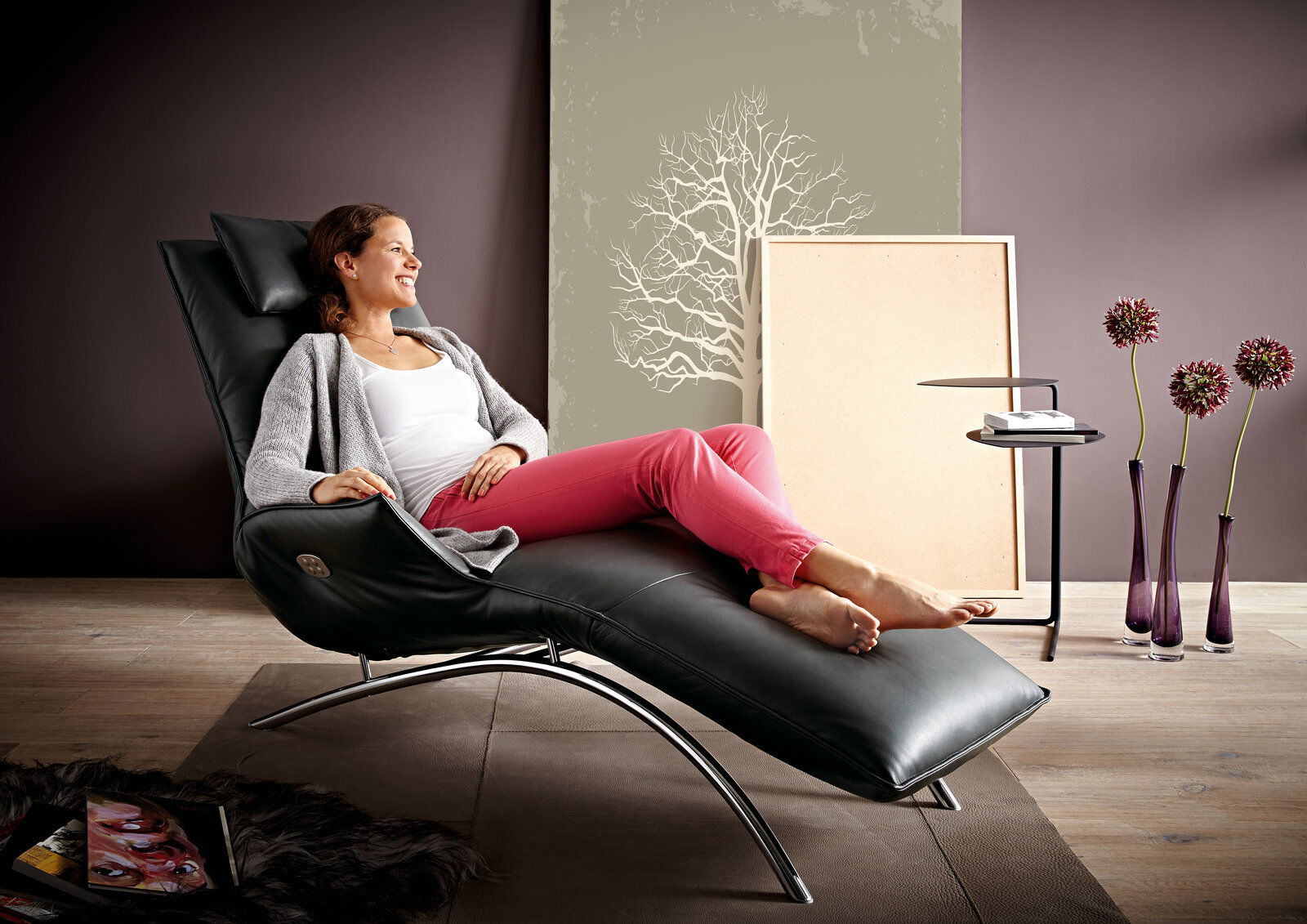 Koinor Funktionsliege JOLEEN Frau entspannt auf einer modernen schwarzen Funktionsliege in einem stilvoll eingerichteten Raum, seitliche Perspektive.