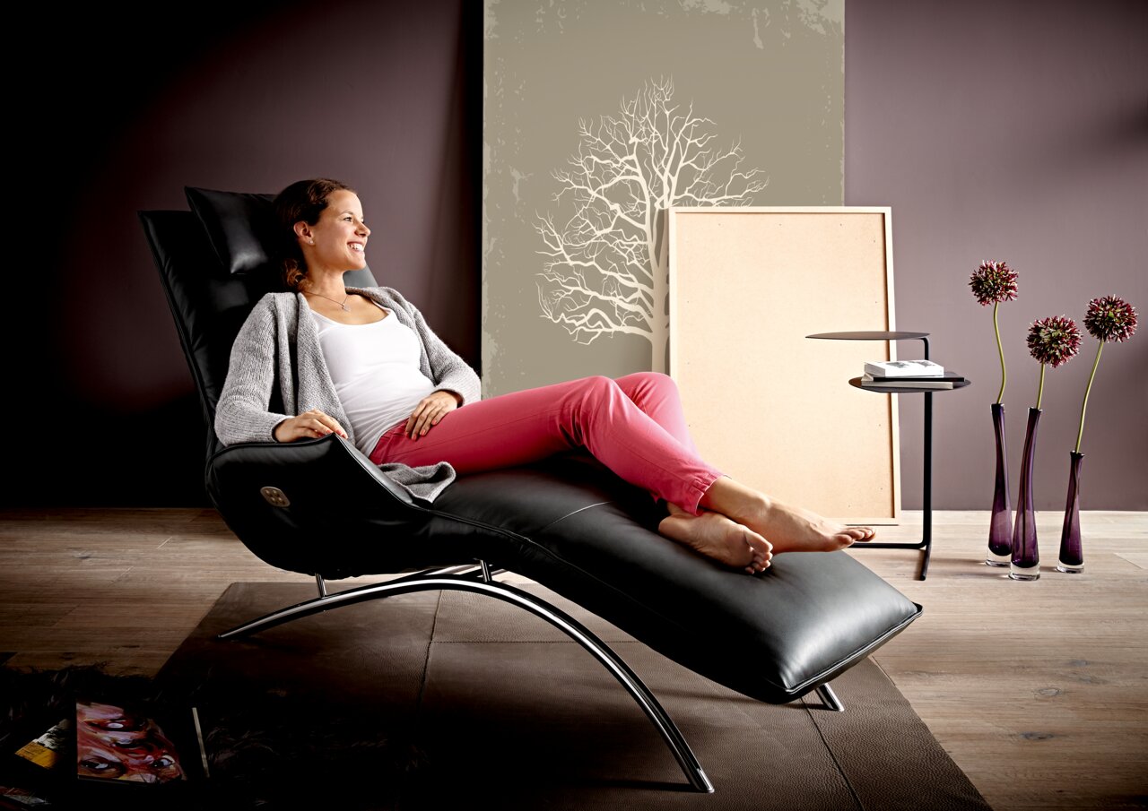Frau entspannt auf einer modernen schwarzen Funktionsliege in einem stilvoll eingerichteten Raum, seitliche Perspektive.