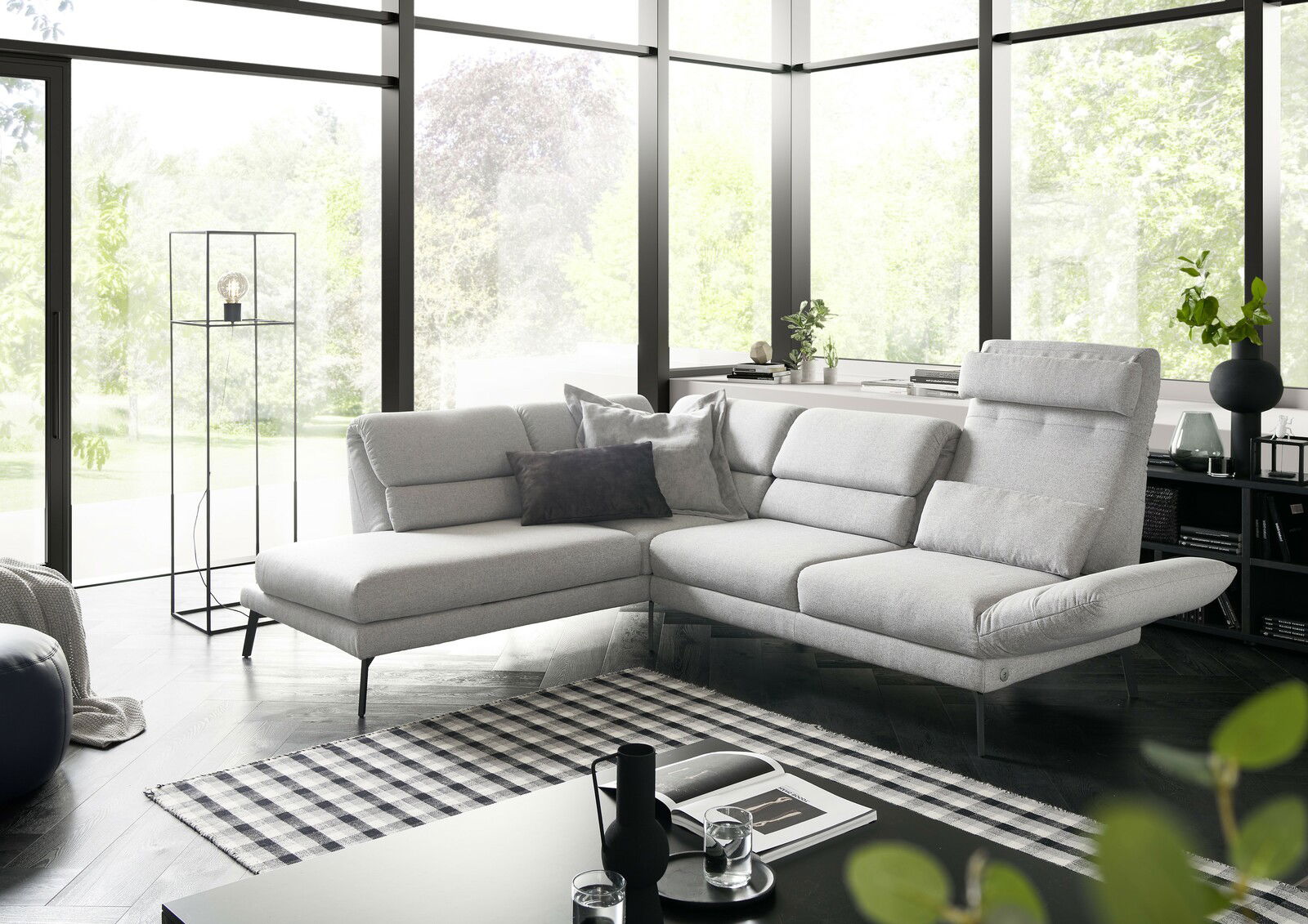 Moderne graue Eckgarnitur in einem hellen Wohnzimmer mit großen Fenstern, seitliche Perspektive