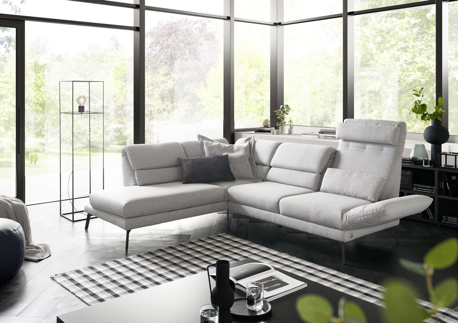 Moderne graue Eckgarnitur in einem hellen Wohnzimmer mit großen Fenstern, seitliche Perspektive