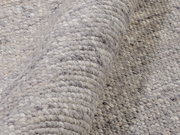 Nahaufnahme eines handgewebten Teppichs in Grautönen, der eine detaillierte Ansicht der Textur und Webart zeigt.