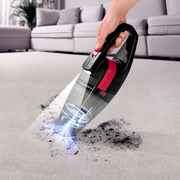 Akku Handstaubsauger in Aktion, der Schmutz von einem Teppich aufsaugt, seitliche Perspektive