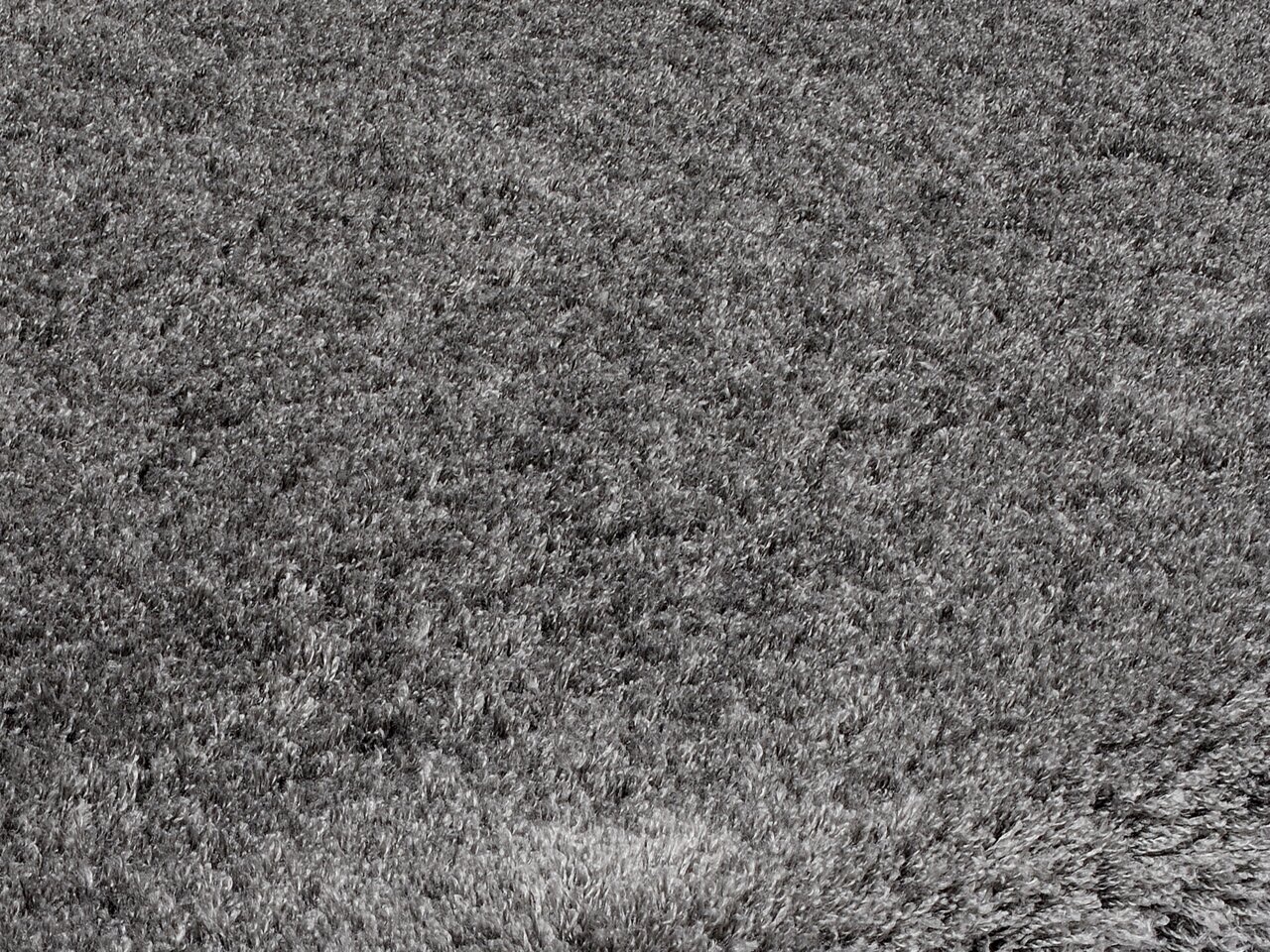 Nahaufnahme eines grauen Hochflor-Teppichs aus der Vogelperspektive.