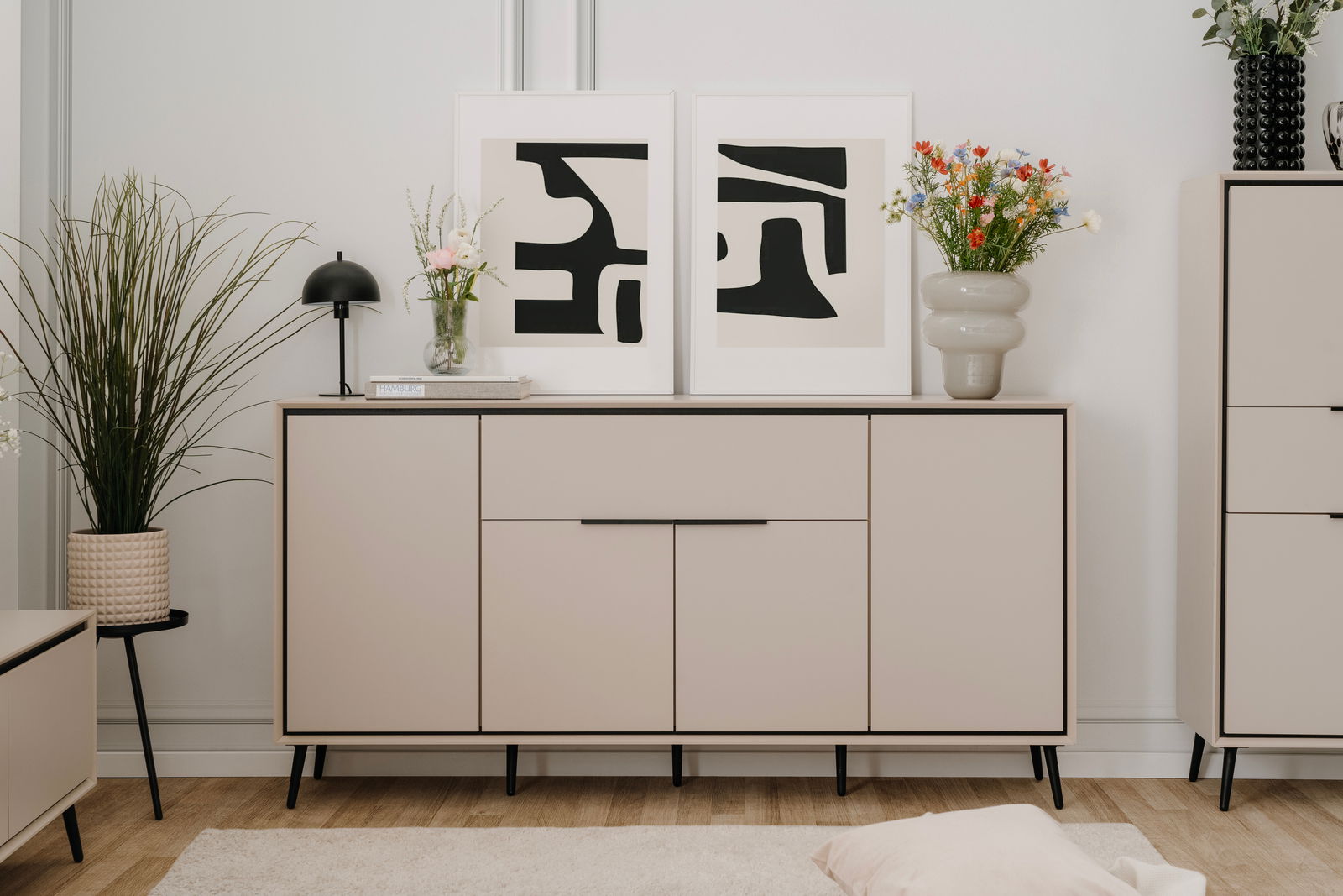 Z2 Dressoir ARONA Modernes Sideboard in hellem Beige mit schwarzen Beinen, dekoriert mit Pflanzen und abstrakten Kunstwerken, Frontalansicht.