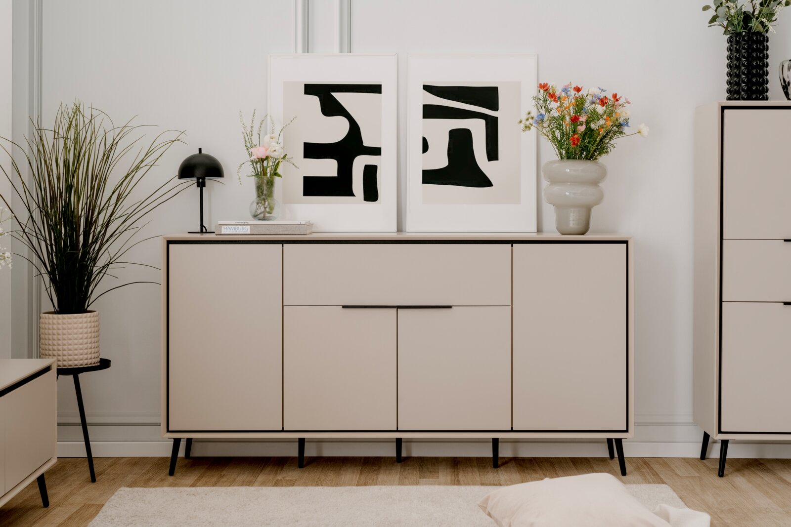 Z2 Dressoir ARONA Modernes Sideboard in hellem Beige mit schwarzen Beinen, dekoriert mit Pflanzen und abstrakten Kunstwerken, Frontalansicht.