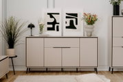 Modernes Sideboard in hellem Beige mit schwarzen Beinen, dekoriert mit Pflanzen und abstrakten Kunstwerken, Frontalansicht.