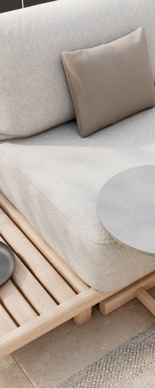 Detailfoto van een hoekbank met lichte stoffen bekleding, beige kussens en houten elementen, gefotografeerd vanuit een schuine hoek van bovenaf.