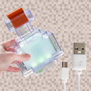 Hand hält transparentes, würfelförmiges LED-Gadget mit orangefarbenem Schalter; daneben weißes USB-A-auf-USB-C-Kabel, Ansicht schräg von vorne/oben