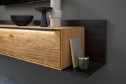 Nahaufnahme einer modernen Wandkombination mit Holzoptik und LED-Beleuchtung, dekoriert mit einer Vase, einer Schale und einem Buch, seitliche Perspektive.