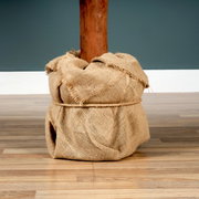 Close-up van de voet van een Tiaga-spar, omwikkeld met jute, staande op een houten vloer.