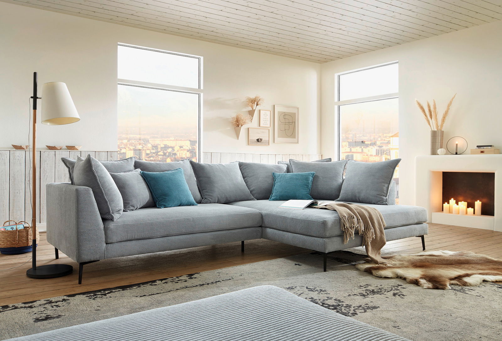 Moderne Eckgarnitur in einem hellen Wohnzimmer mit großen Fenstern, dekoriert mit blauen und grauen Kissen, aus der Perspektive von vorne links.