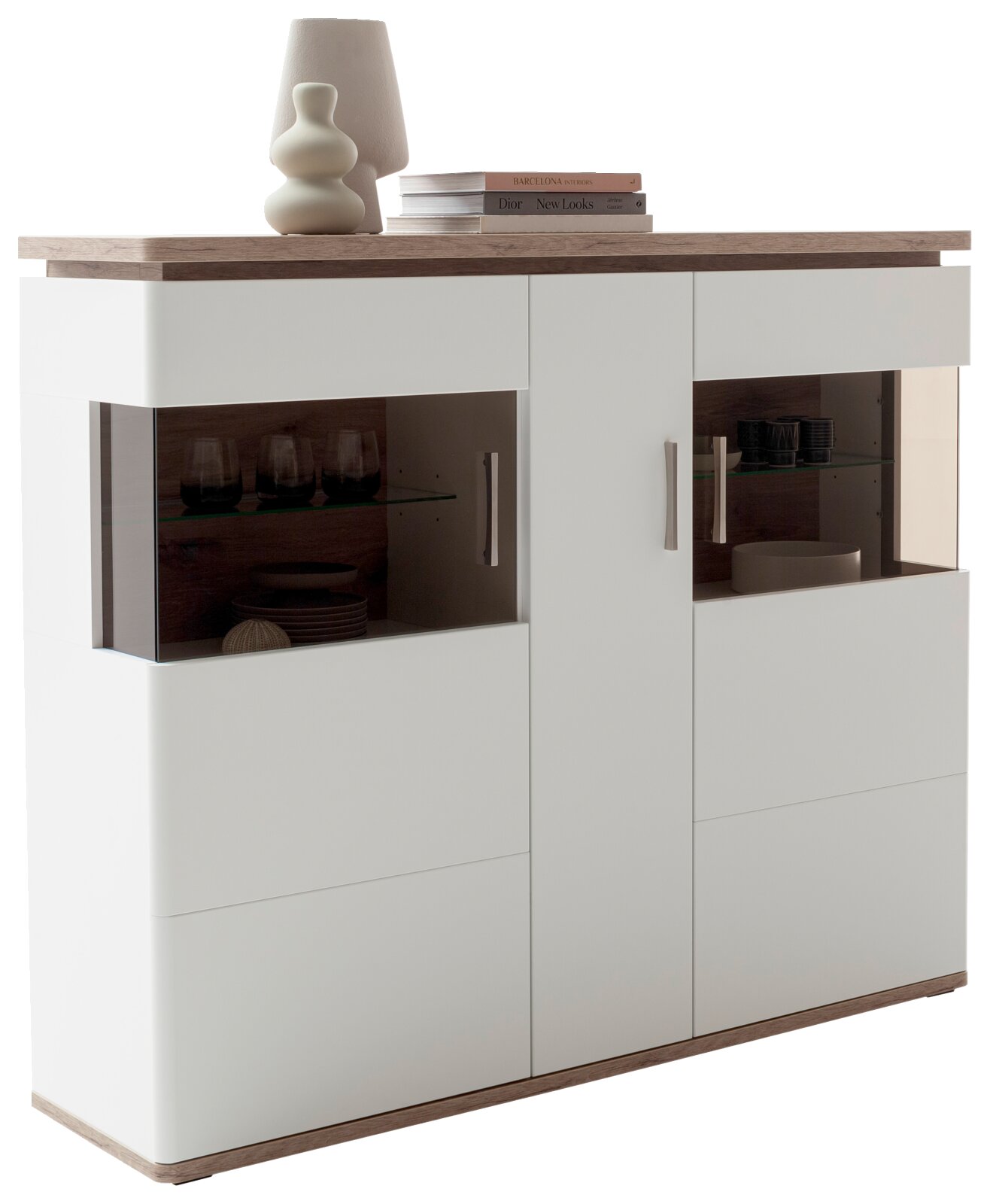 Moderne weiße Vitrine/Highboard mit Holzoptik-Deckplatte und -Sockel, mittleren Türen und seitlichen Glasvitrinen mit Glaseinlegeböden und Metallgriffen, fotografiert in leicht schräger Frontansicht von links.