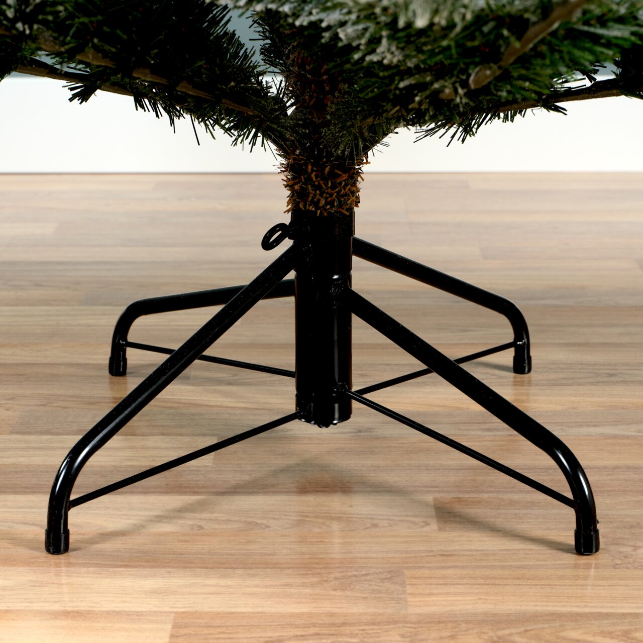 Nahaufnahme eines stabilen Metallständers für einen Weihnachtsbaum auf einem Holzboden, seitliche Perspektive.