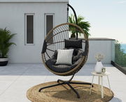 Moderner Hängesessel auf einer Terrasse, seitliche Perspektive, mit Kissen und einem kleinen Beistelltisch mit Vase und Getränk.