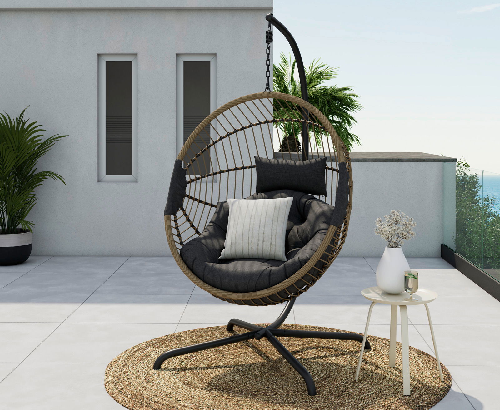 Moderner Hängesessel auf einer Terrasse, seitliche Perspektive, mit Kissen und einem kleinen Beistelltisch mit Vase und Getränk.